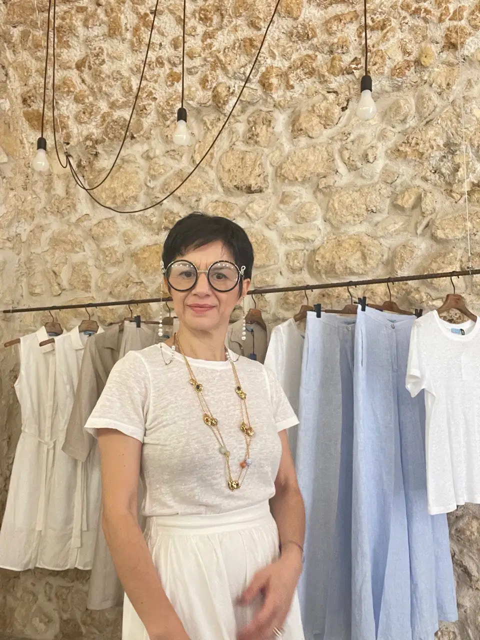 Maria Chiara Pizzo nel negozio Just Noto, con i capi esposti e la parete in pietra